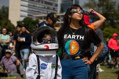 A boy in an astronaut costume and a girl observe the annular solar eclipse wearing eclipse glasses at the facilities of the National Autonomous University of Mexico in Mexico City on October 14, 2023