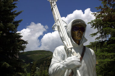 a bronze statue of a man wearing a white hood carrying skis
