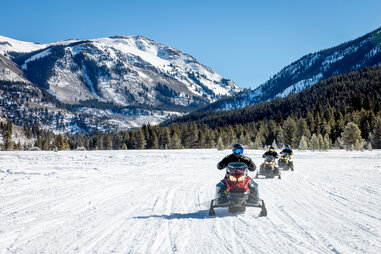 people on snowmobiles surrounded by the Rocky Mountains