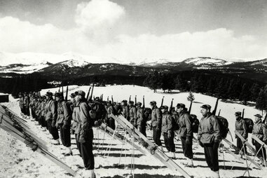 10th mountain division soldiers standing at attention on a mountain, with skis lined up in front of them