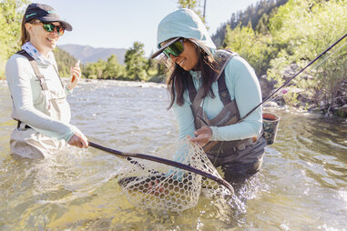 female fishing guide helping angler with brown trout in net montana