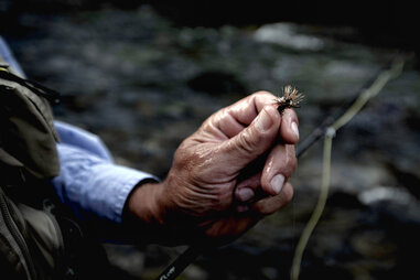 man holding fly to tie on rod for fishing adventure