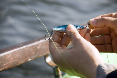 person tying a lure onto fishing line rod and reel