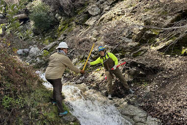 hiking trail workers in angeles national forest pass equipment across a stream