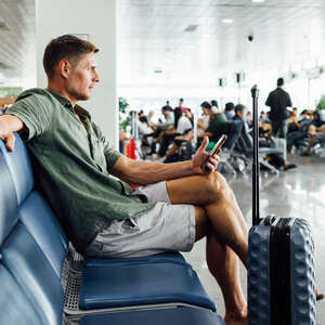 Casual mature man with smartphone waiting at airport terminal seating area