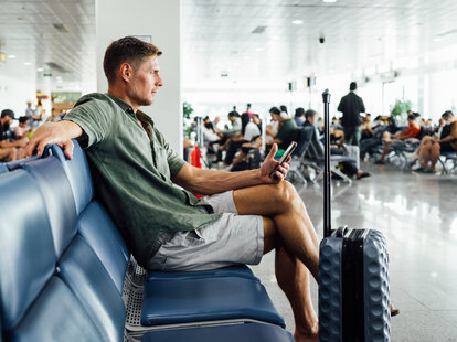 Casual mature man with smartphone waiting at airport terminal seating area