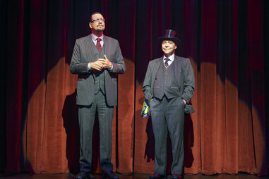 two men in pinstripe suits standing on stage. One has a top hat.