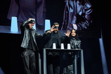 a man with his hands held over three styrofoam cups, flanked by a man and a woman