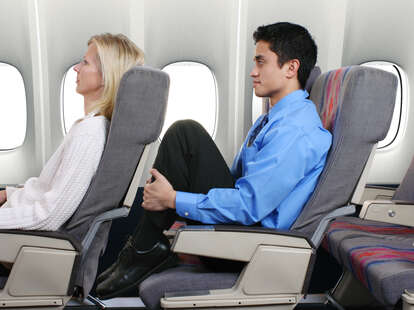 An airplane passenger dramatically depicting what having no leg room on a flight is like.