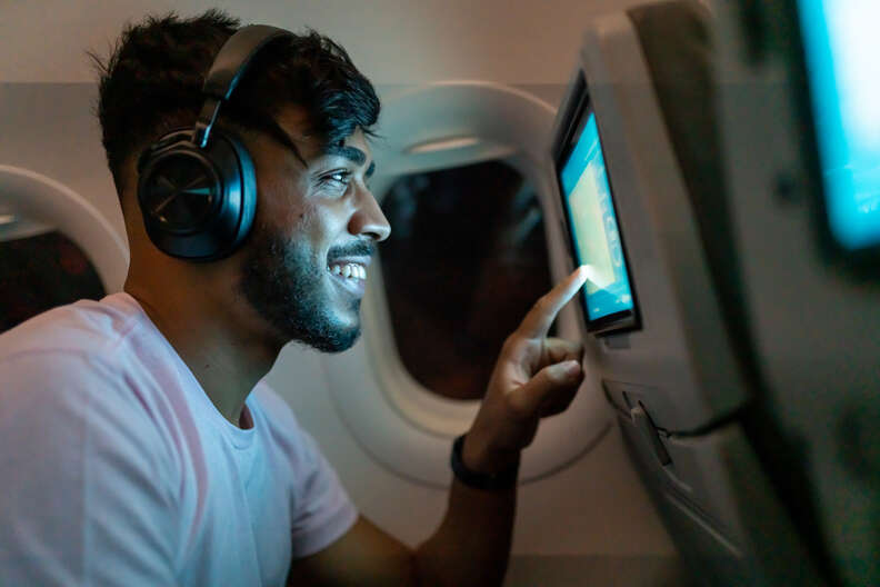 A smiling man choosing what he's about to watch on a plane screen