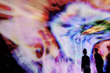 people looking at a wall with a trippy rainbow tie dye projection 