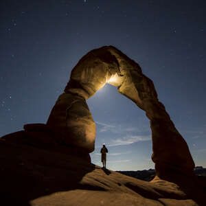 A backpacker standing underneath Delicate arch in Arches National Park, Utah
