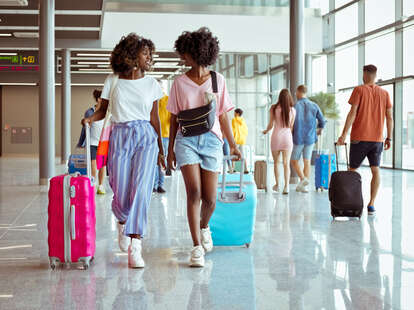 Passengers walking with wheeled luggage at airport terminal.