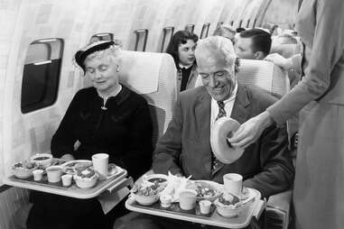 a vintage photo of people looking at plane food in a Boeing 707
