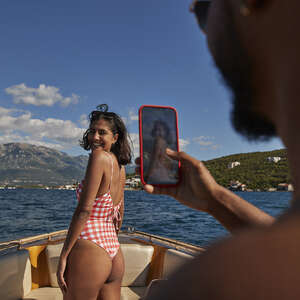 Young woman in swimwear photographed by man on smart phone during sunny day.