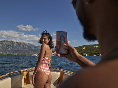 Young woman in swimwear photographed by man on smart phone during sunny day.