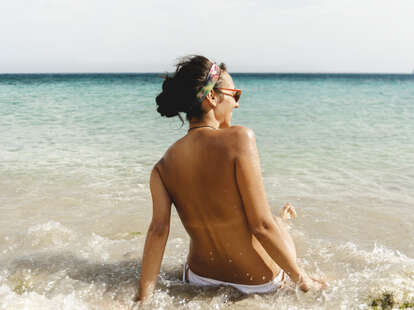 Rear view of shirtless woman sunbathing at a beach.