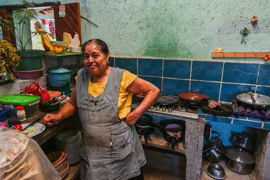 local oaxacan woman standing in front of stove in comedor with tiled background