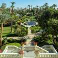 A large and beautiful multi leveled garden with sculptures, a small pool, palm trees, and manicured lawns.