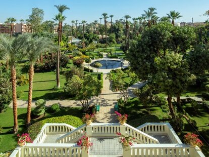 A large and beautiful multi leveled garden with sculptures, a small pool, palm trees, and manicured lawns.