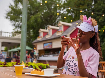 A woman wearing Minnie Mouse ears headband, taking photo of her food at Epcot.