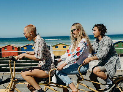 Three friends laughing on a tandem bicycle on a boardwalk