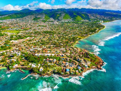 The suburban residential districts of Honolulu, Hawai’i along the coastline just outside of downtown from about 1000 feet over the Pacific Ocean.
