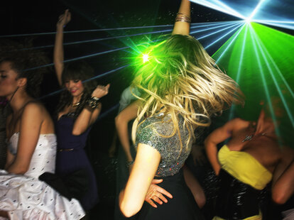 Group of young people dancing in nightclub with laser lighting wearing dated clothing.