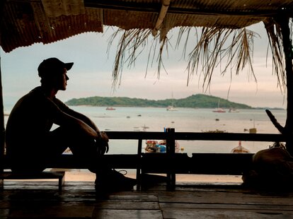 A man outlined in shadow sitting on the beach in Phuket, Thailand.