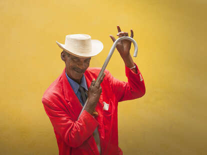 cuban male dancer in red suit posing with a cane on yellow background