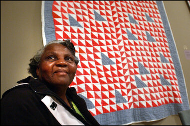 woman posing in front of red white and blue quilt from gee’s bend