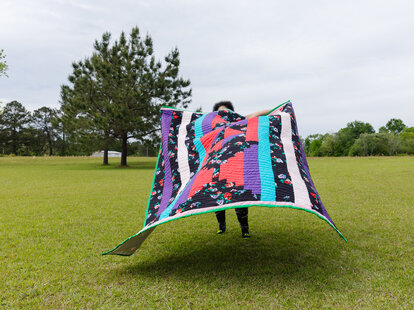 woman holding quilt from gee’s bend quilting collective in alabama while standing in a field