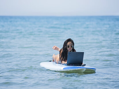A young woman is working on a surfboard with her laptop, in summer at Hayama in Japan.