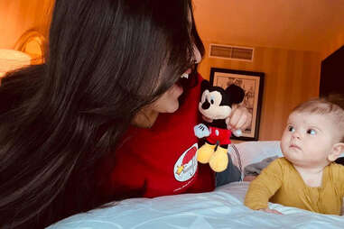 woman playing with baby and mickey mouse doll in hotel room 