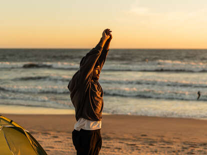 Young man stretching and camping on the beach in the early morning.