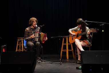 duo playing accordion and guitar on a dark stage with stools