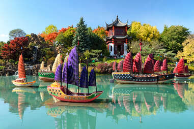 beautiful view of a turquoise pond and a traditional chinese pavilion and boats within a botanical garden