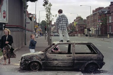 Young children play on a burnt out car after a bomb attack in the Lower Ormeau road area in Belfast on July 14, 1996.