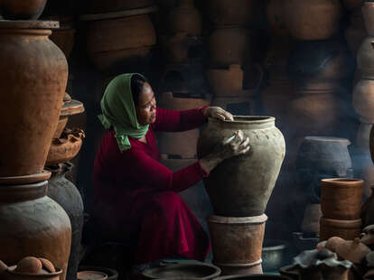 woman with headscarf crafting pottery vessel in darkness