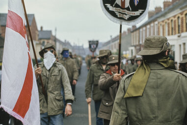 Masked members of the Ulster Defence Association (UDA), a Loyalist paramilitary organisation, dressed in military jackets, during a parade with banners and a Red Hand of Ulster flag in Belfast, Northern Ireland, circa 1973.