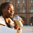 Young woman drinking an iced latte from disposable cup standing in town square during daytime