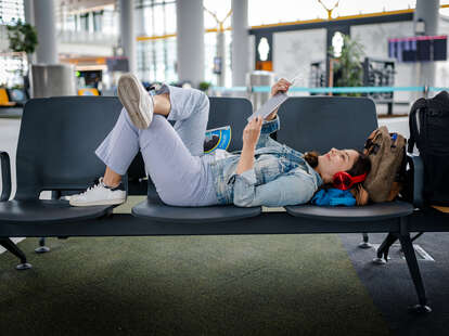 Young Woman waiting for delayed flight and reading digital book on chairs.