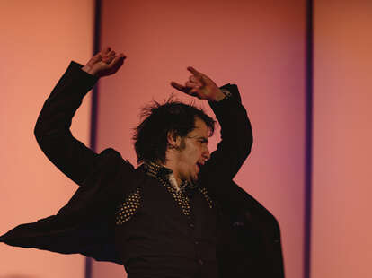 a sweaty man dancing flamenco, with his arms thrown up in the air 