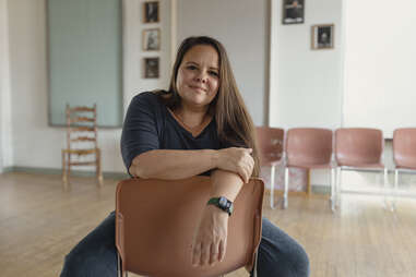 a woman, Marisol Encinias, sitting in backwards in a chair, smiling