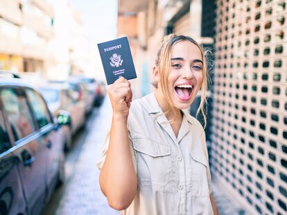 Young woman smiling happy outdoors on a sunny day showing USA passport.