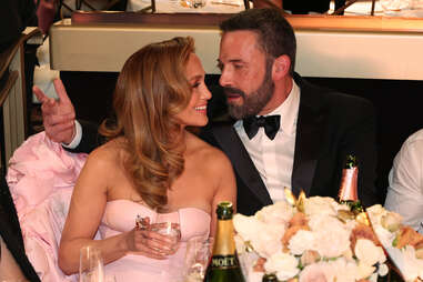 two people, Jennifer Lopez and Ben Affleck, sitting at the Golden Globes awards ceremony and looking at each other. She wears a pink dress