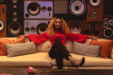 a woman in a red shirt and black pants sitting on a couch in front of speakers