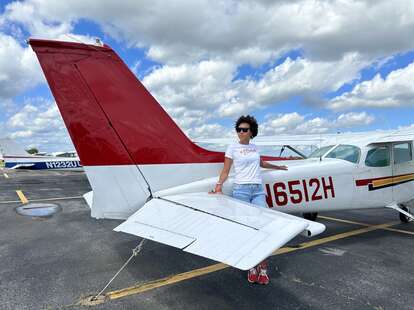a woman standing in front of a small red and white Cessna plane