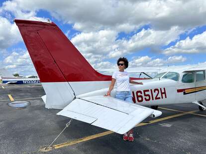 a woman standing in front of a small red and white Cessna plane 