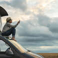 woman sitting on top of car searching for service on her cellphone 